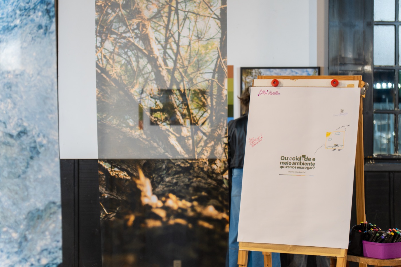 Painel interativo da exposição Cidade, Cor e Ambiente, com a pergunta “Que cidade e meio ambiente queremos enxergar?”, ao lado de peças em voil na Galeria Estação da Arte, em Passo Fundo.